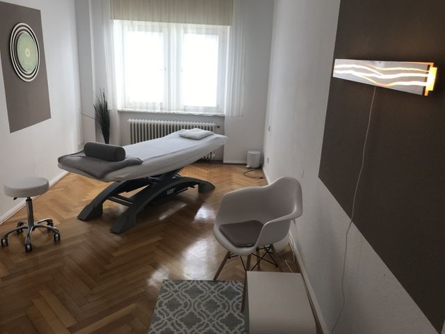 Behandlungsraum in Heidelberg mit Behandlungsliege, hellem Fenster und Parkett